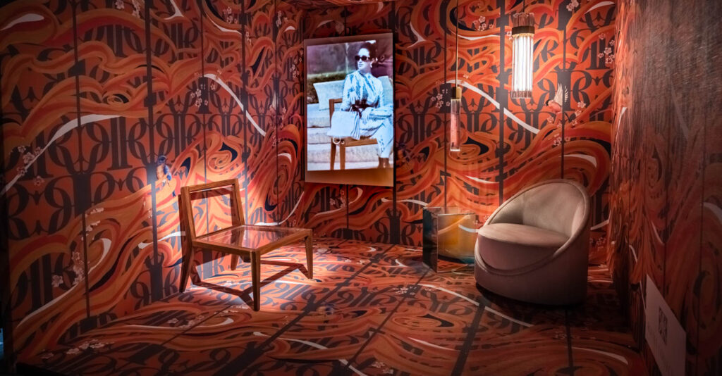 A colorful room with two sitting chairs and a film playing.